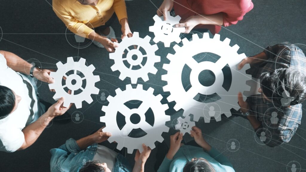 People holding interlocking gear cutouts, symbolising teamwork and collaboration.